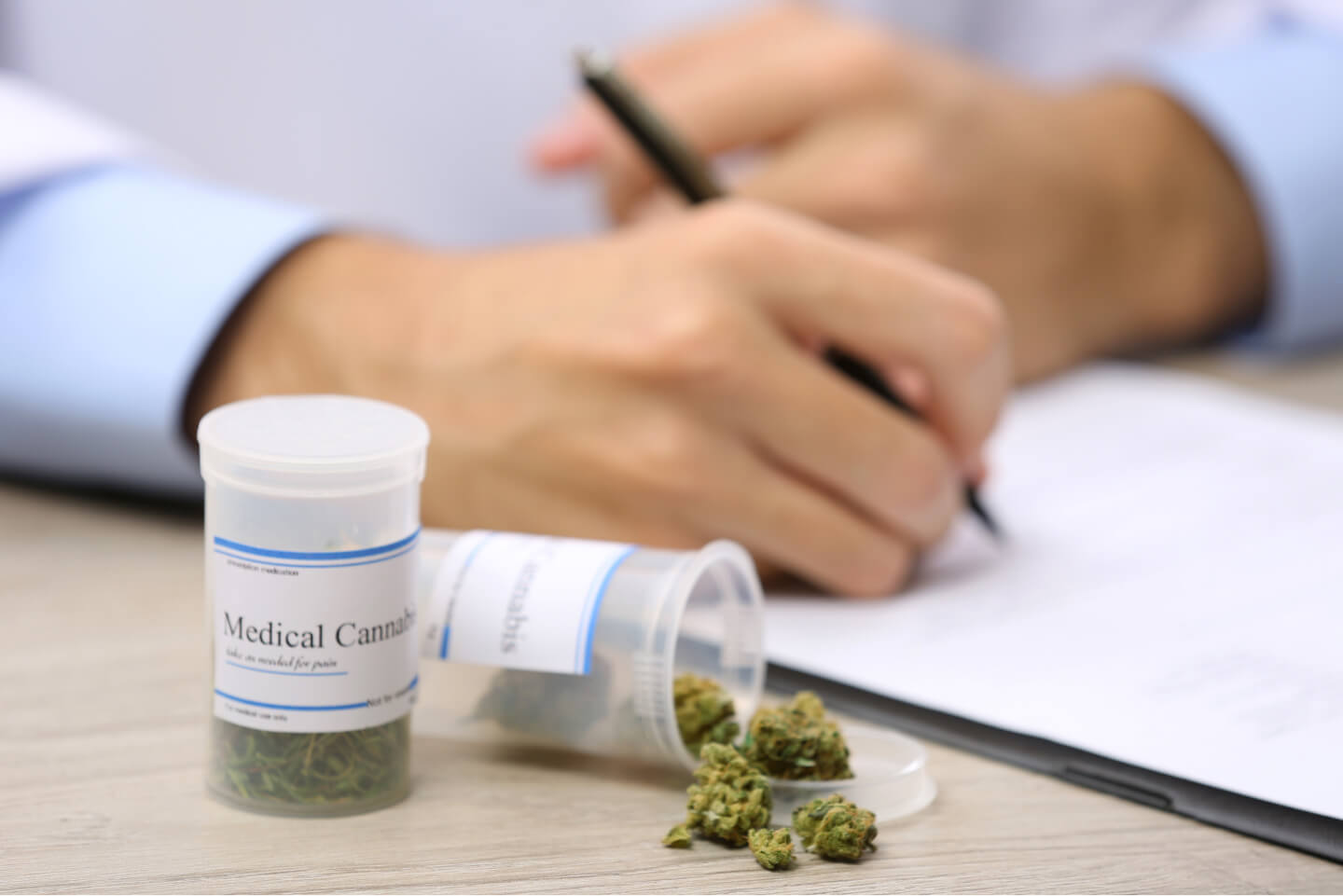 Medical Cannabis Rezept mit Cannabis-Blüten in Apotheken-Dosen, Hand mit Stift im Hintergrund